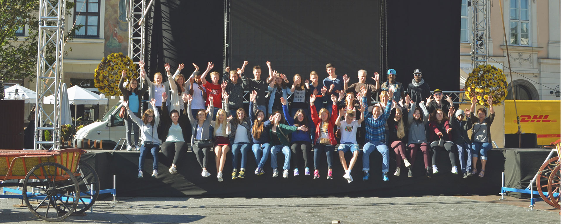 Bilde av elever og lærere på skoletur i Krakow, de sitter på kanten av en scene på gaten ute - Kristen Videregående Skole Nordland - E-sport