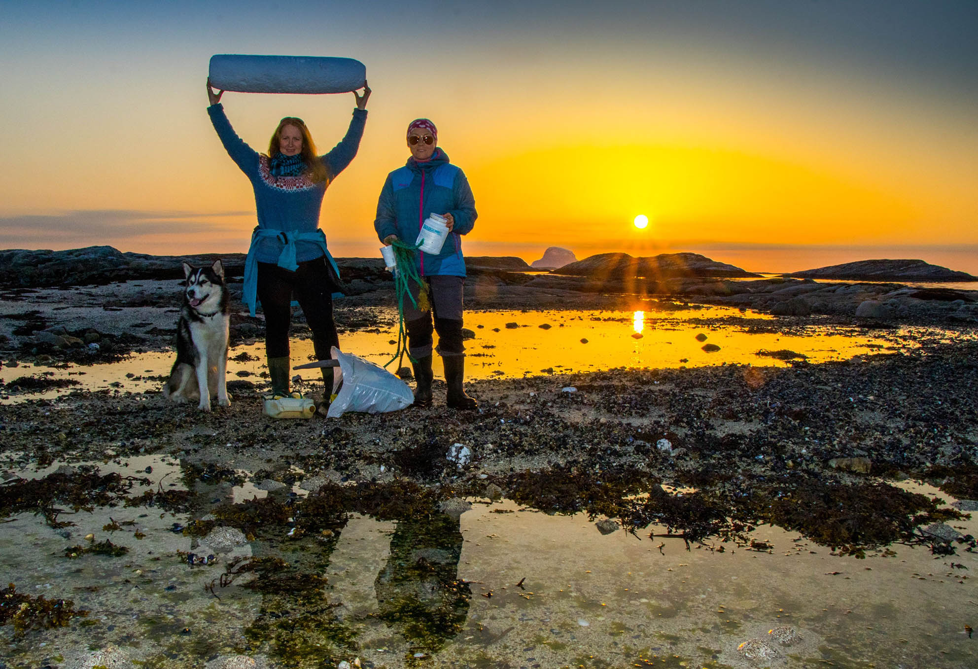 Bilde av to kvinnelige lærere og en hund med rase husky, de står på en type strand ved vannet under solnedgang - Kristen Videregående Skole Nordland - E-sport