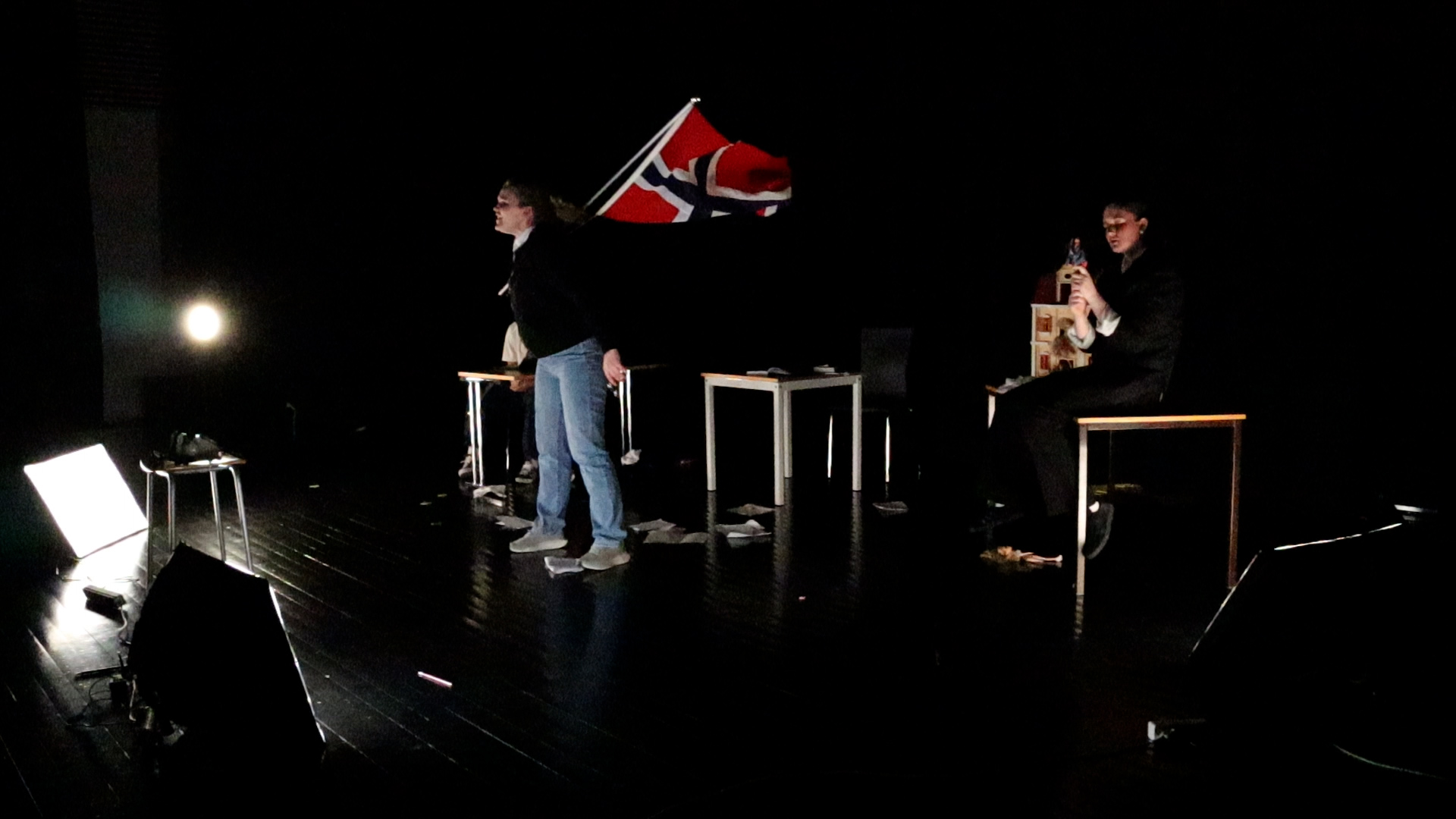Tre elever på en scene fremfører et teaterstykke, hvor en slenger på et norgesflagg de to andre sitter bak