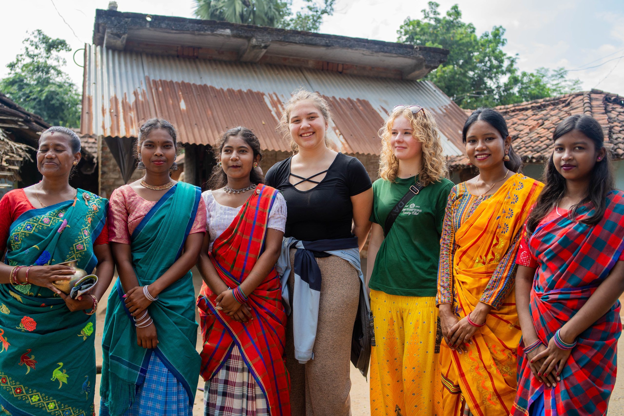 To elever som står sammen med fem indiske damer i fargerike klær