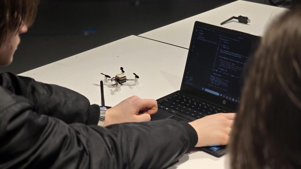 En elev som skriver kode på en bærbar datamaskin med en drone ved siden av