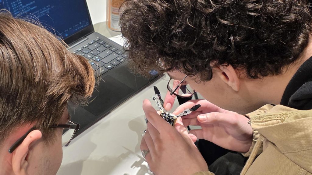 Bakhodet til to elever som undersøker en liten drone som ligger i hånden deres.