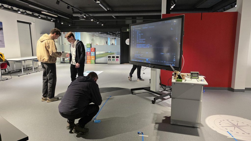 To elever som står å ser på en drone, mens en annen sitter på huk for å se på en drone.