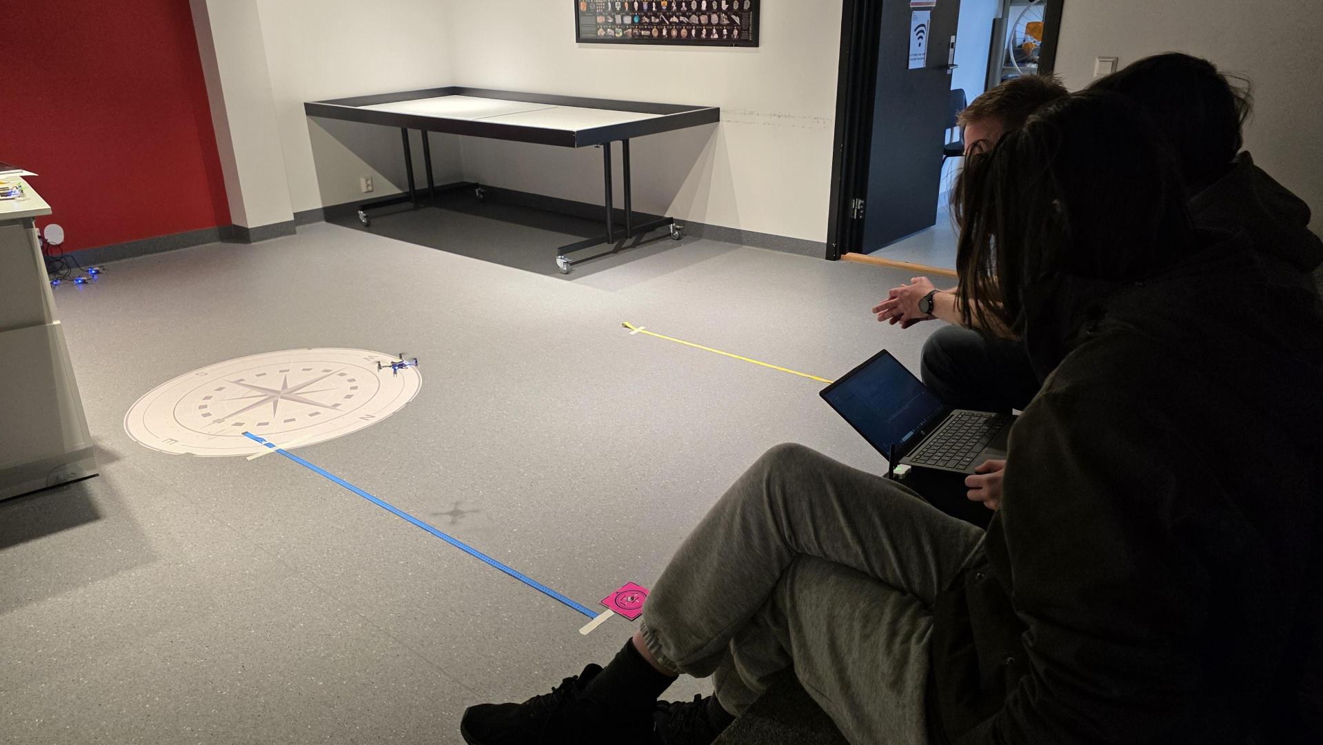 Tre elever som sitter rundt og ser på en pc. På gulvet ligger det to målebånd i to forskjellige farger