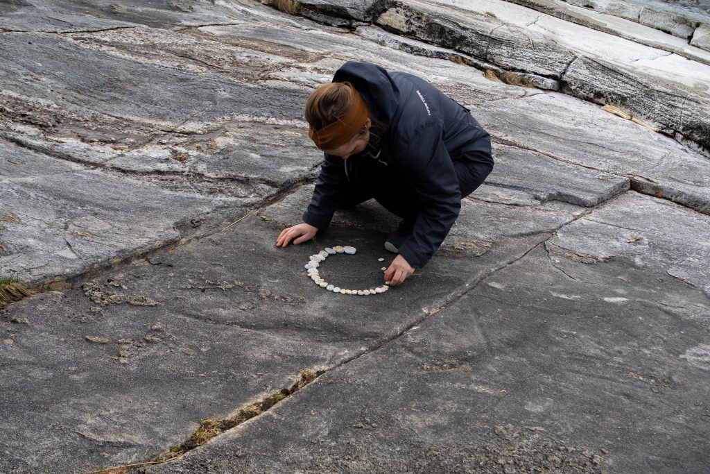 Lærer som sitter på et berg og lager landart med hvite steiner
