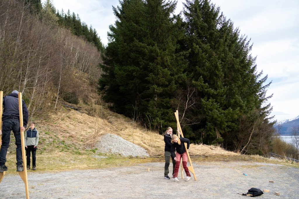 Elever på avstand som prøver å gå på stylter på en parkeringsplass