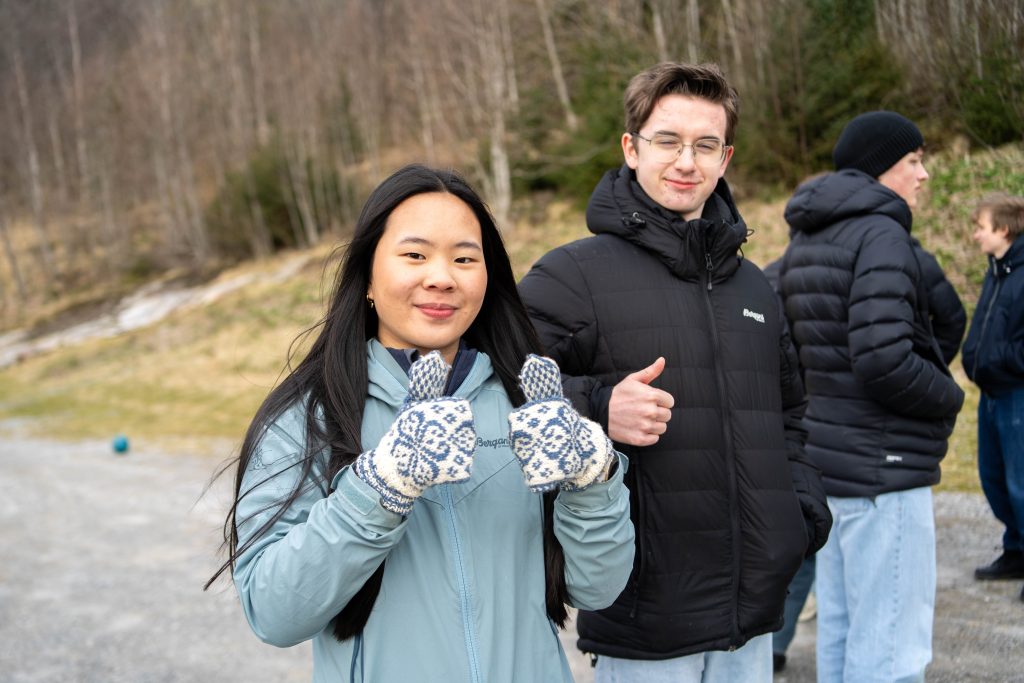To elever som står og gir tommelen opp til kamera med små smil om munnen