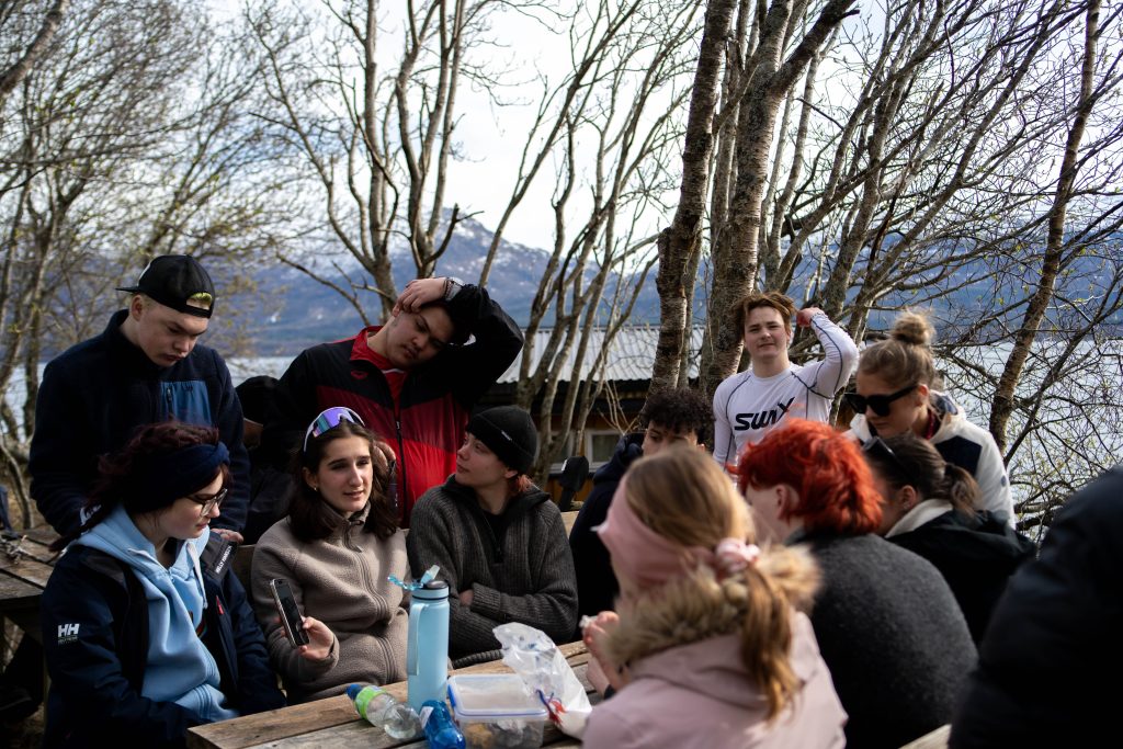 En større gjeng som sitter rundt et utebord og prater med en del ting på bordet